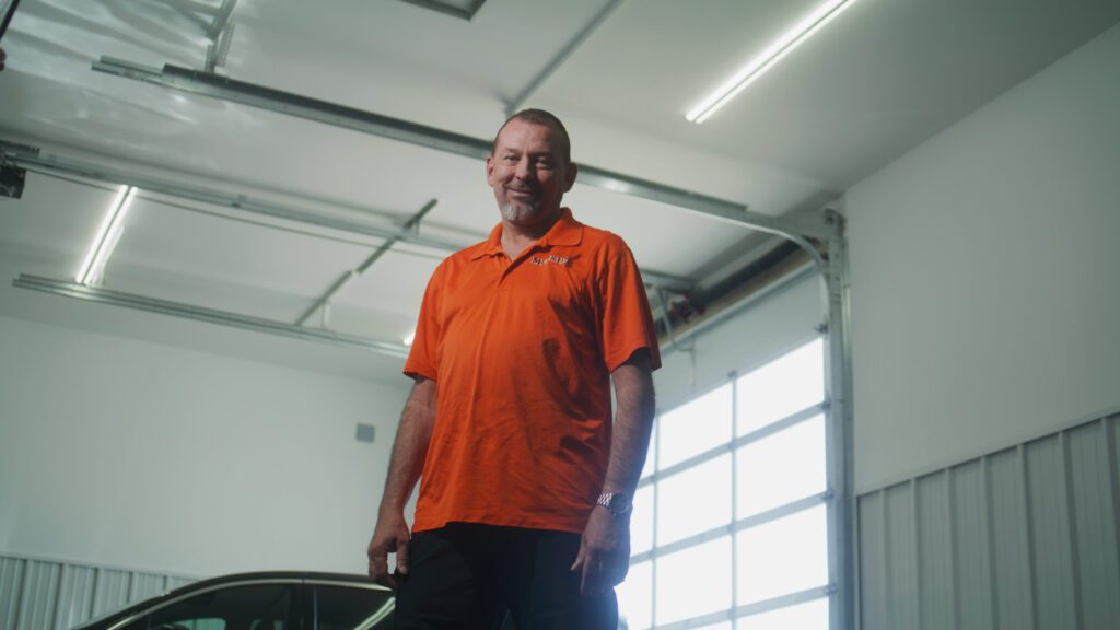 MedRide driver Mr. Harris standing in a service bay, wearing an orange MedRide polo.