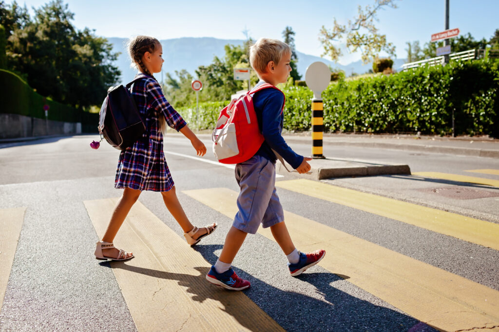 Two students with backpacks crossing the street safely, representing MedRide's student transportation services in Colorado.