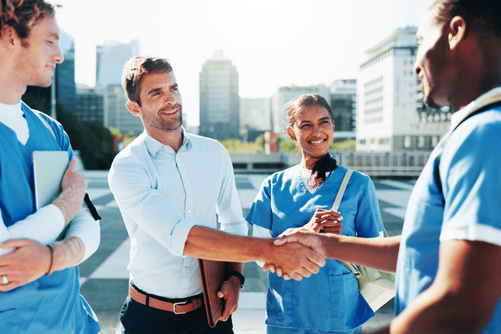 Healthcare staff and a transportation provider shaking hands outside a medical facility to coordinate patient transportation services